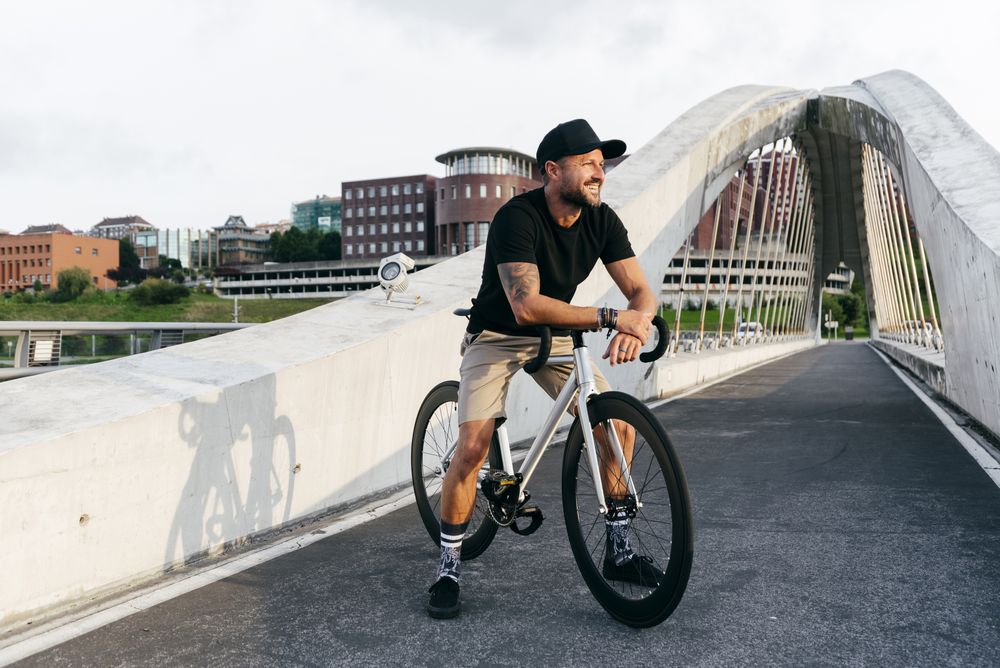 Cheerful man with bicycle standing on footbridge