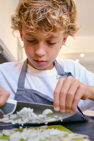 Crop attentive boy cutting raw onion in house kitchen