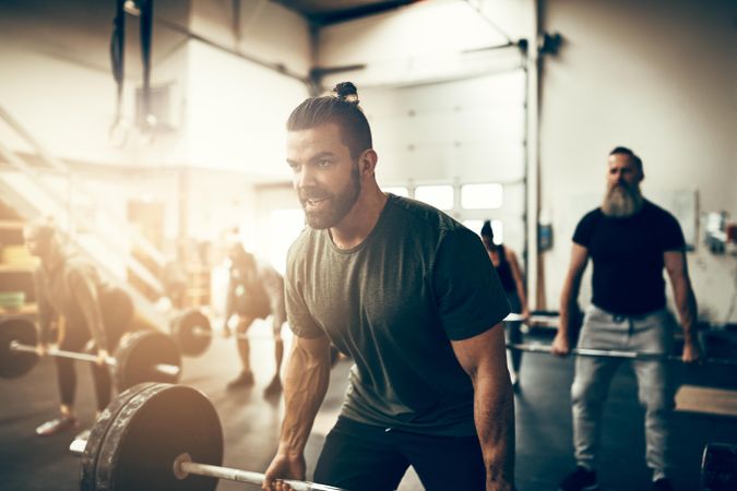 Focused man lifting heavy barbell in busy gym
