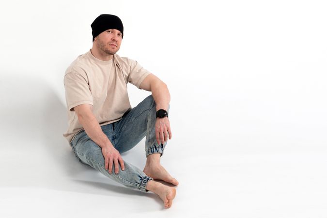 Man in beige t-shirt and beanie sitting barefoot
