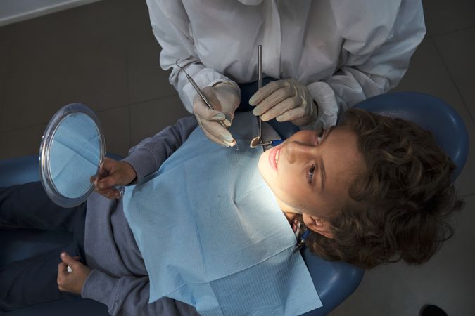 Dentist in medical uniform examining teeth of boy in clinic