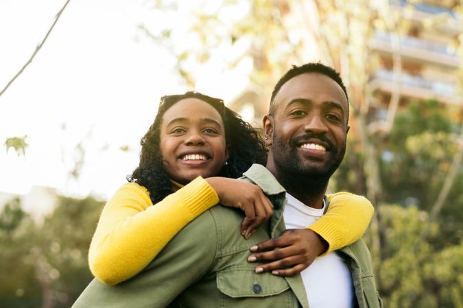 Portrait of a smiling Black man giving piggyback ride to his sister