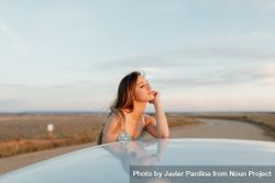 Young woman resting her head on her chin on roof of car bGRee4