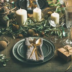 Festival holiday table setting, with gold ornaments, branches, and crystal flute, square crop