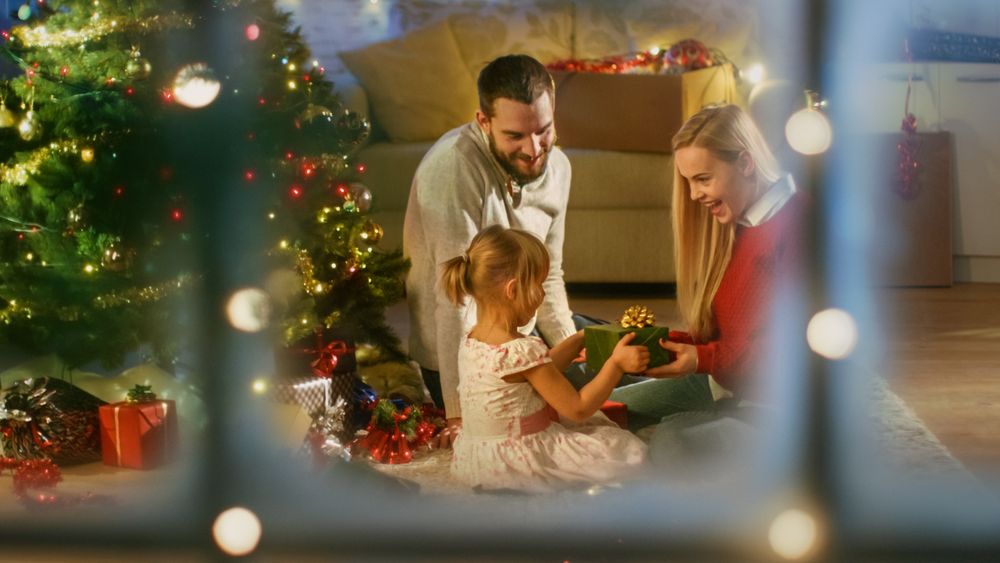 Looking Through Snowy Window at Father, Mother and Daughter Sitting Under Christmas Tree.