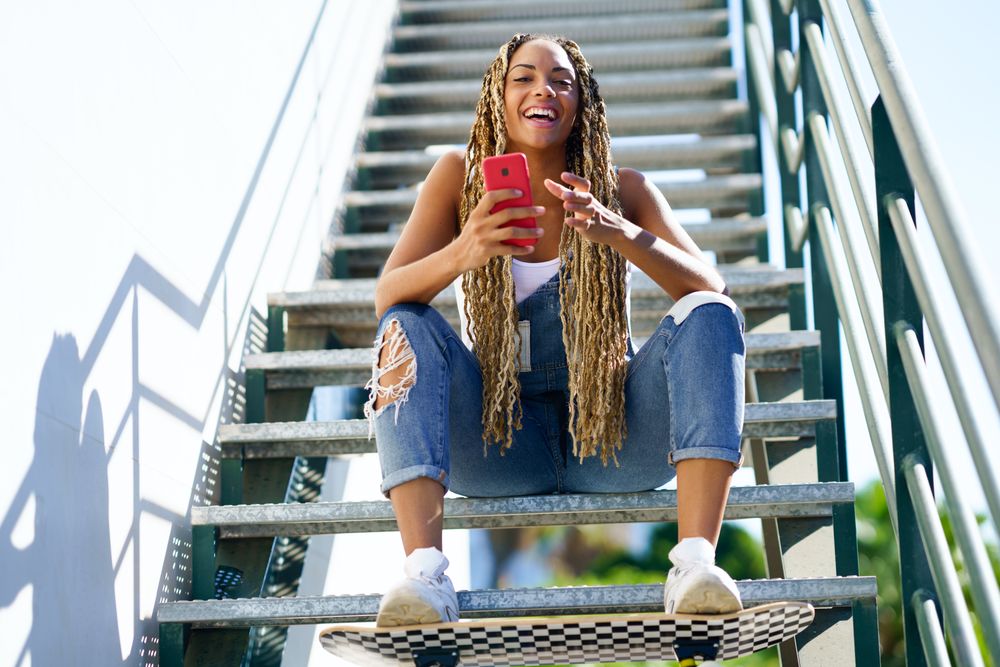 Laughing female skater checking phone on stairs