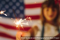Kid playing with fire sparkles with the American flag in the background 5zBaQ5