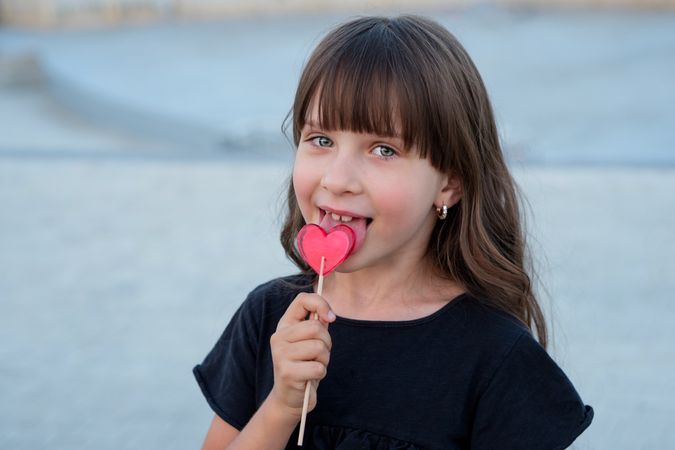Funny little girl with red heart shaped lollipop