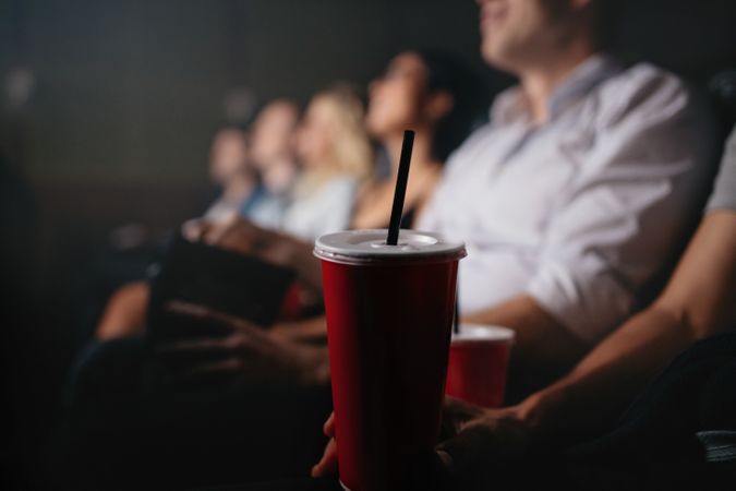 Close up shot of young people with soft drinks in movie theater, focus on cold drink glass