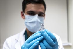 Gloved hands holding COVID vaccine vial