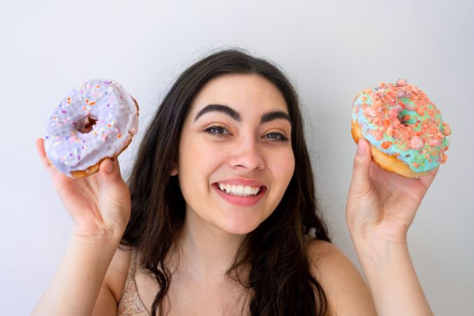 Playful woman making glasses of donuts while standing by white wall