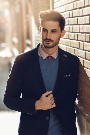 Man leaning on brick wall outside wearing elegant suit