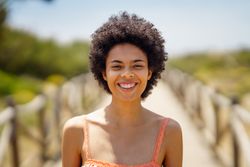 Portrait of smiling woman with afro hair standing on wooden footpath by the coast