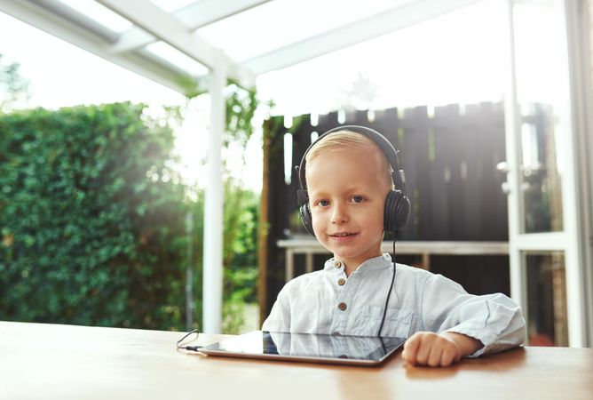 Smiling blond boy using headphones listening to something on digital tablet
