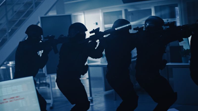 Masked Team of Armed SWAT Police Officers Move in Row in a Hall of a Dark Seized Office Building with Desks and Computers.