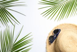 Composition with straw hat, sunglasses and palm leaves on light background. Top view, space for text