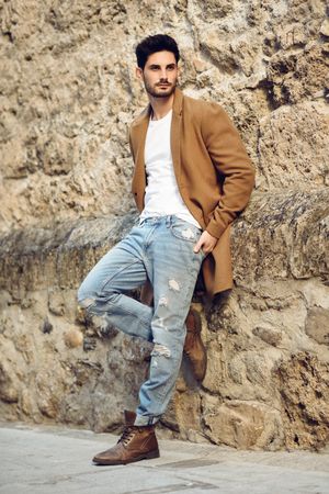 Man in winter jacket and jeans leaning on wall outside