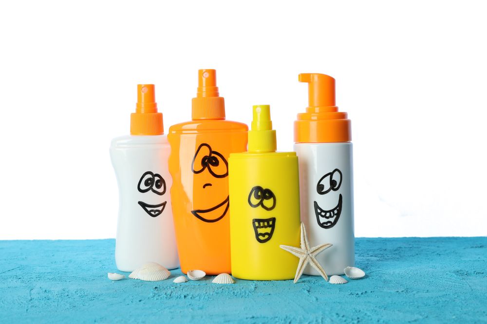 Happy sunscreen sprays with starfish and seashells on color table isolated on blank background. Safe tan