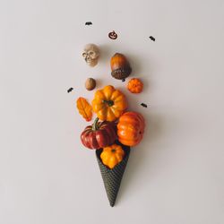 Pumpkins and halloween decorations in dark ice cream cone on light background