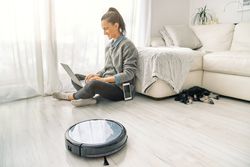 Female freelancer using laptop and sitting on floor near robotic