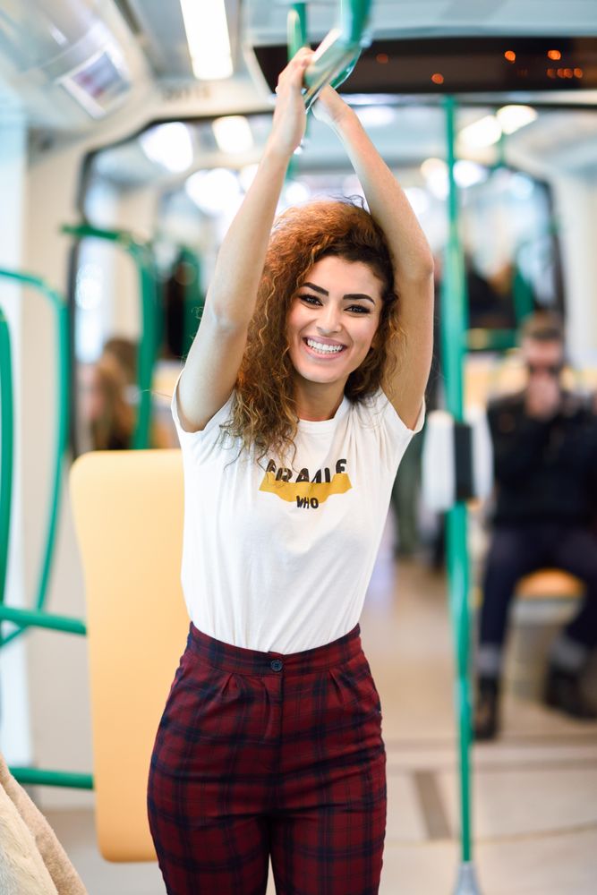 Happy Arab woman holding bar above head in subway carriage