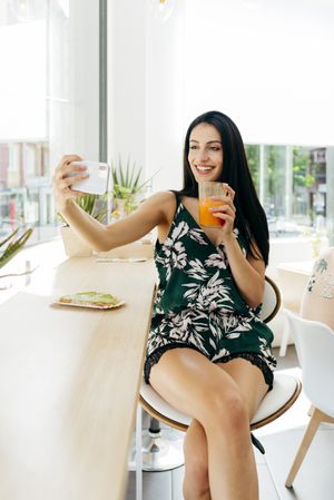 Woman with healthy drink taking selfie in cafe