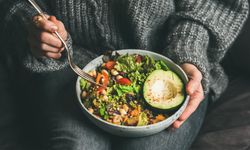 Woman in jeans and sweater holding bowl of fresh salad