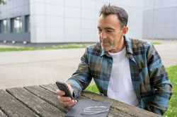 Concentrated man with smartphone and laptop in park