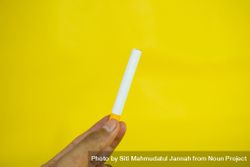 Fingers holding cigarette against yellow wall 56G8LN