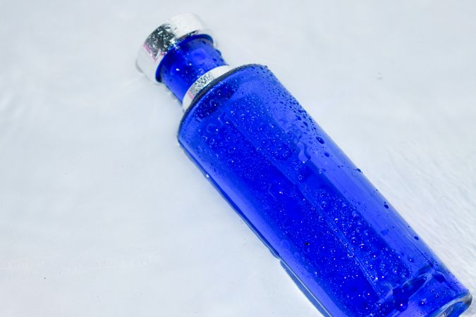 Blue perfume bottle with water droplets on light background