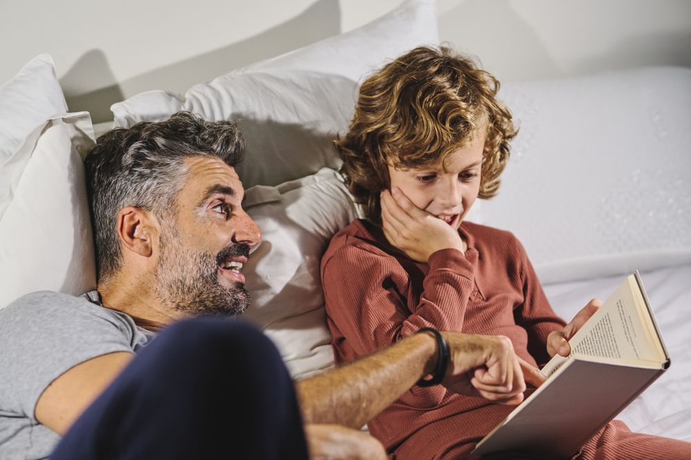 Father and son reading interesting book while lying on bed