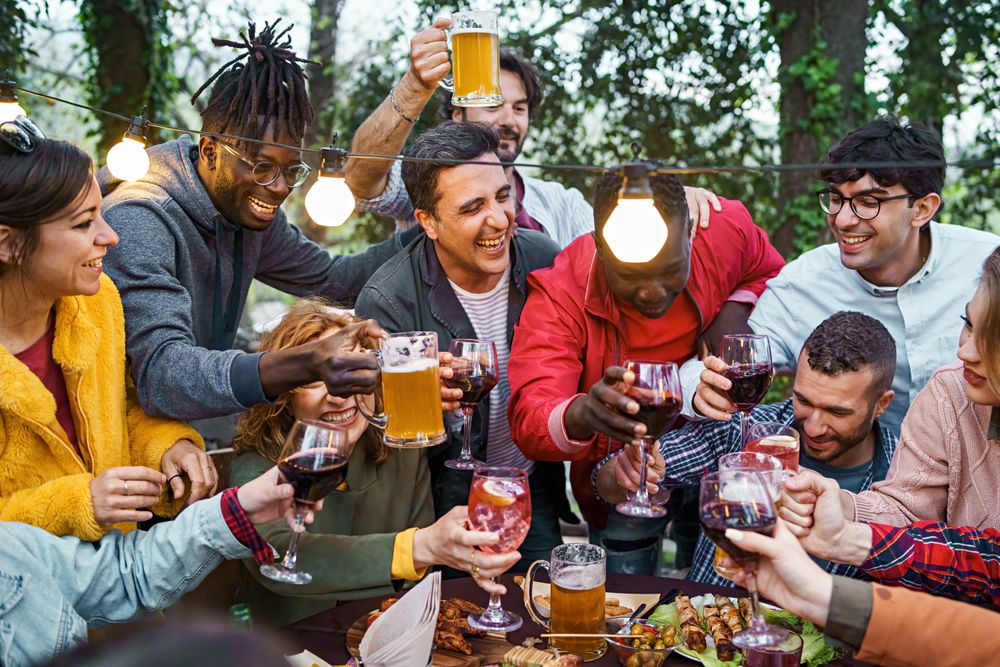 Multi-cultural friends laugh and clink glasses in an outdoor celebration, enjoying a sunny day