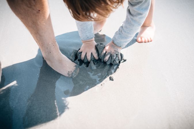 Child with parent kneading sand with hands and feet