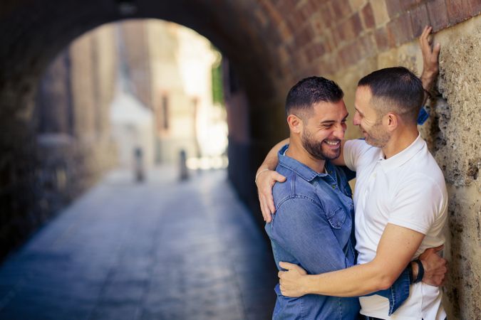 Two men smiling together in an embrace under a city bridge