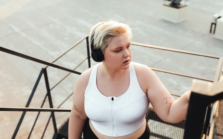 Curvy blond woman wearing headphones on outdoor staircase