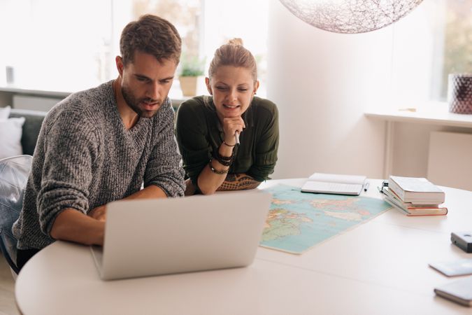 Young man and woman sitting with world map with computer on study table