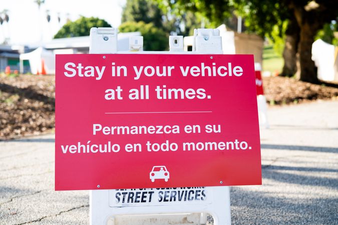 Sign with words “Stay in your vehicle at all times” written in English and Spanish at testing site