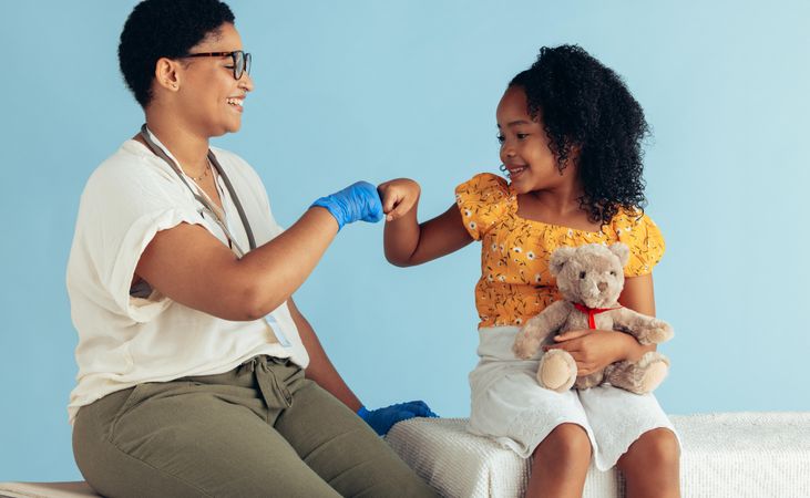 Doctor giving fist bump to girl sitting in clinic