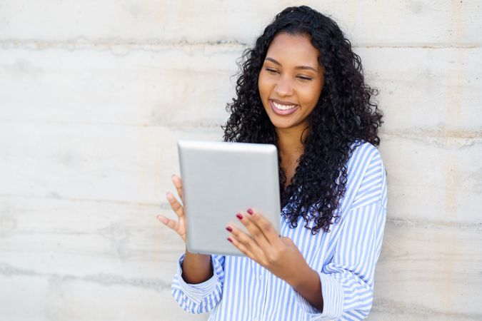 A Young Woman is Engaged with a Digital Tablet While Outdoors, Dressed in Casual Attire