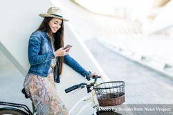 Woman in blue denim jacket riding on bicycle and holding her phone 5oB1G0