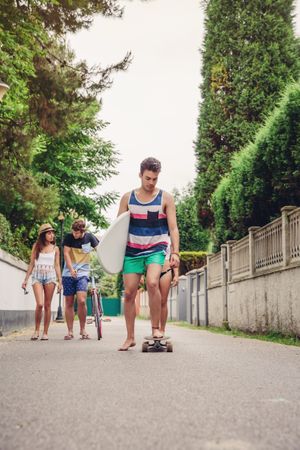 Young man riding on skate and holding surfboard