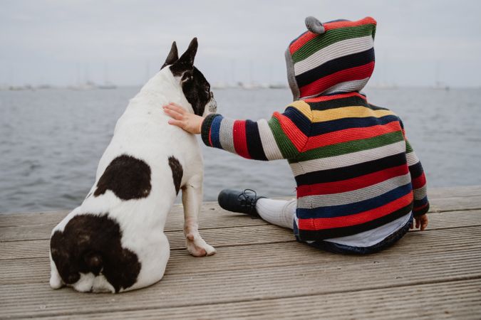 Anonymous kid petting dog on pier