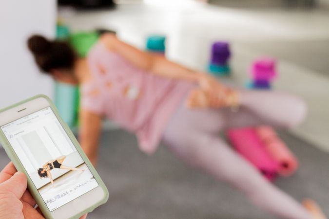 Person holding smartphone against woman doing yoga
