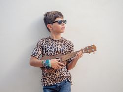 Excited kid raising hands up with ukulele