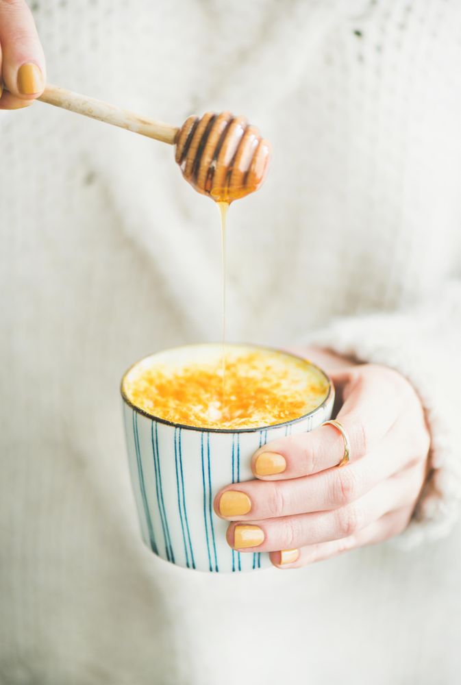 Female using honey dipper to add honey to latte