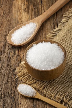 Coarse salt in bowl on wooden background.