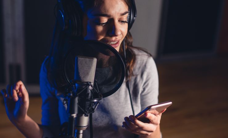 Female singer in front of microphone reading lyrics on her smartphone and recording her song