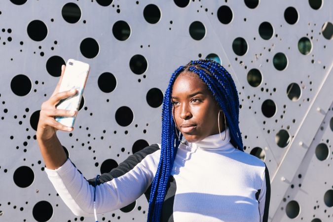 Serious Black woman taking selfie on street
