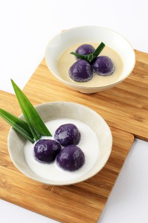 Two bowls of purple sweet potato balls covered in coconut milk sauce