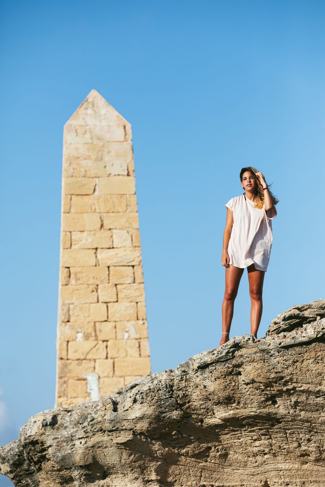 Stylish young woman on vacation getting on top of cliff